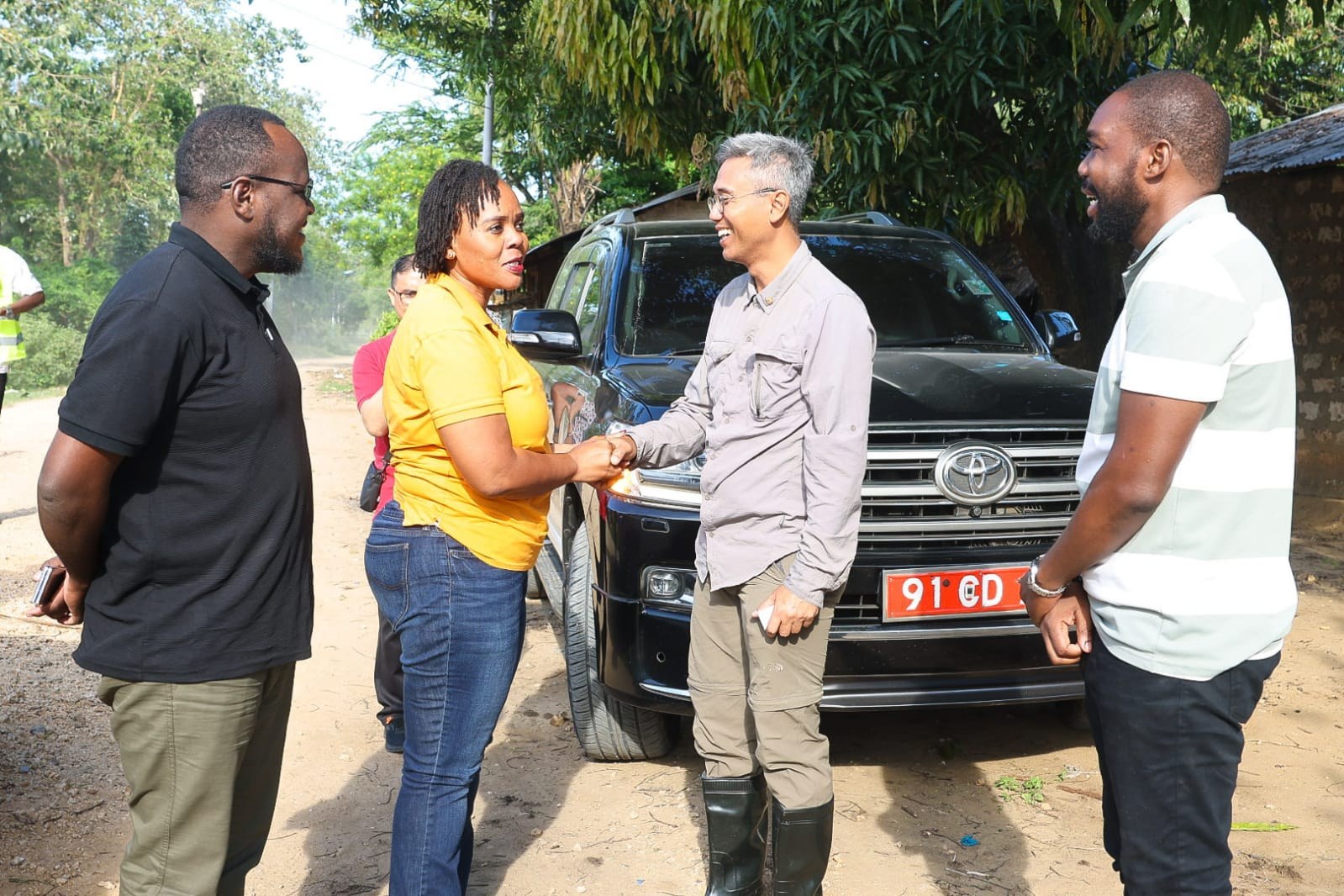 Partners greeting one another with a handshake beside a vehicle during a field visit